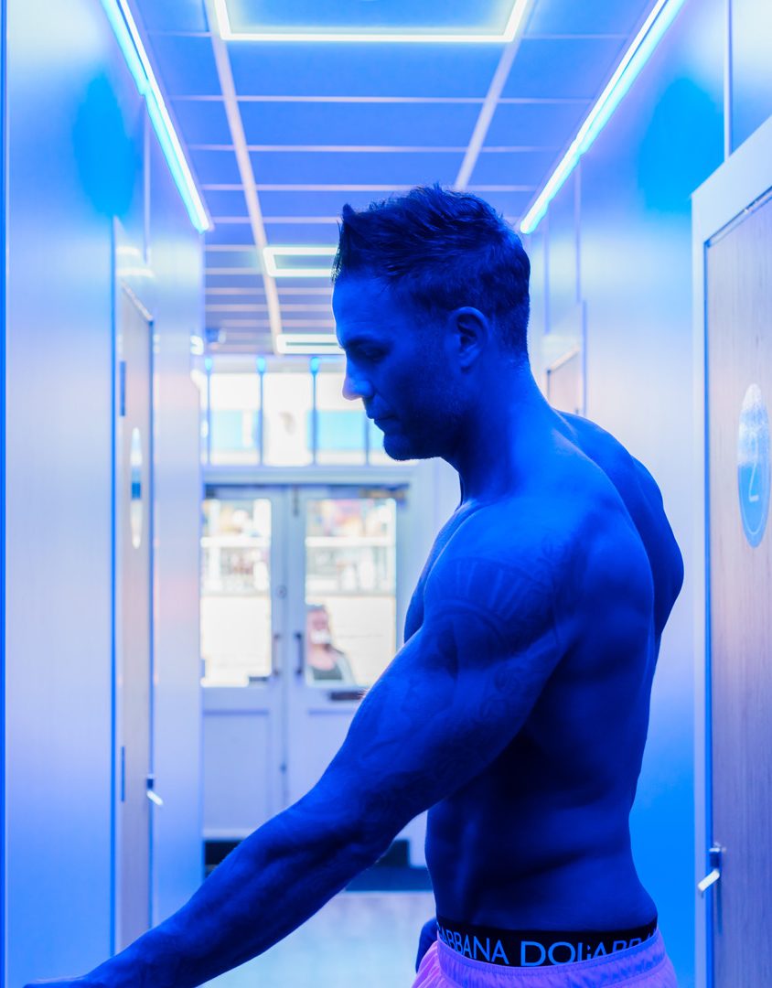 man with his top off in a corridoor about to open a door