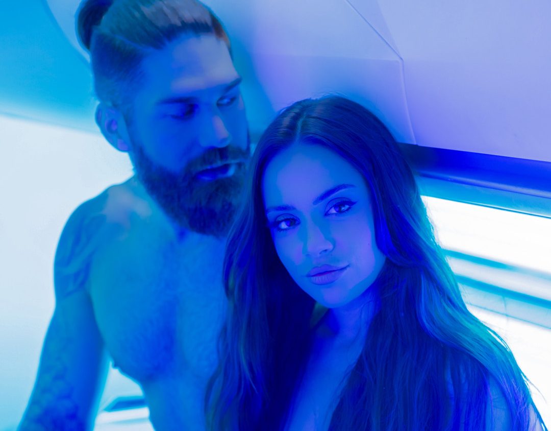 woman in bikini and topless man sat on sunbed in tanning salon