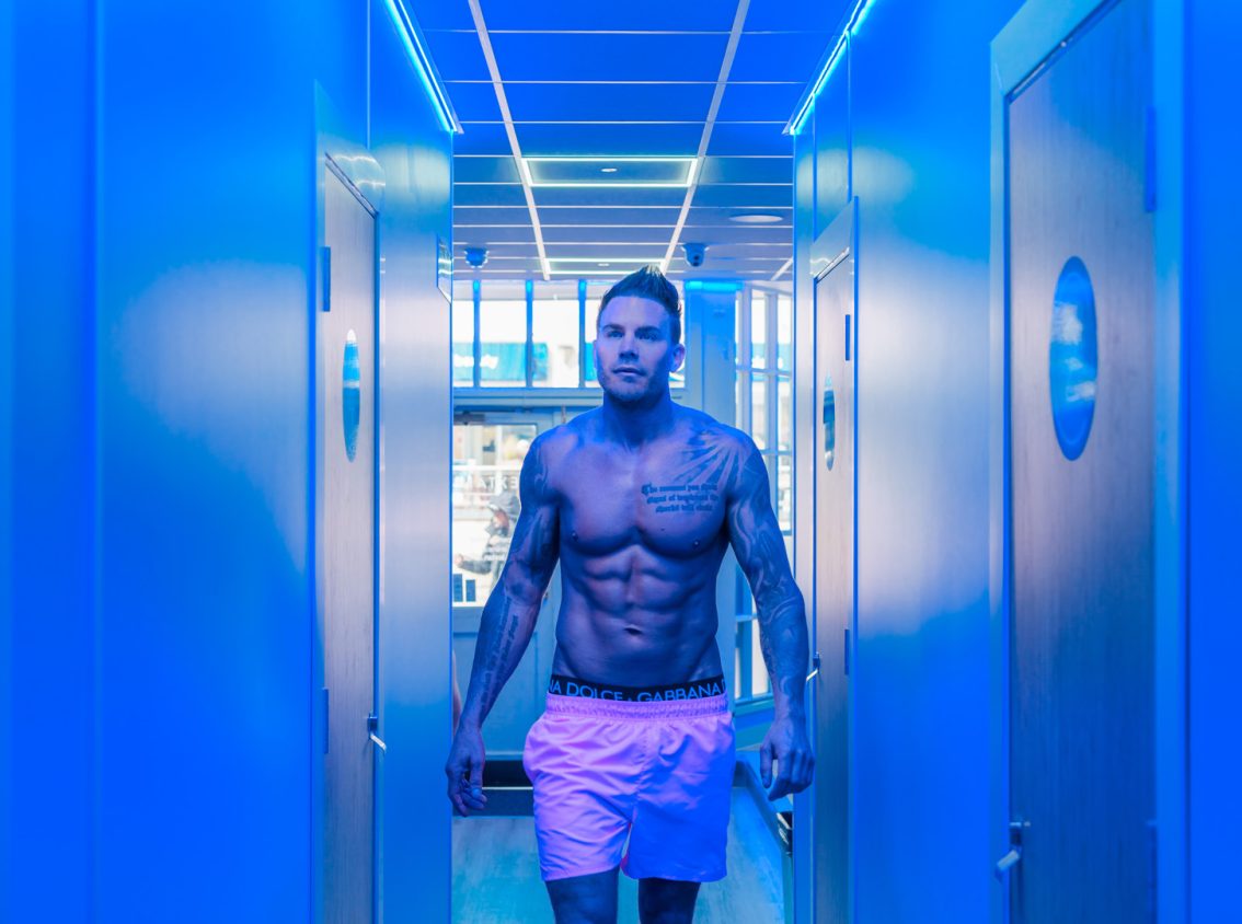 man in pink trunks walking down a corridor